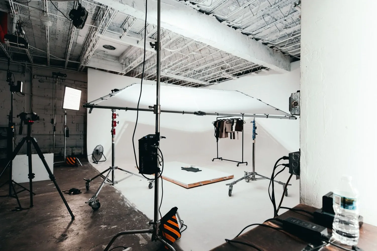Overhead diffusion frame, lights, and a clothing rack on an empty white cyclorama set before a shoot