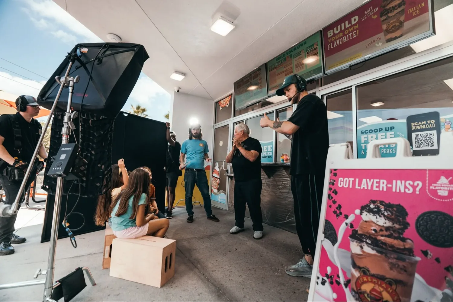 Crew shooting outside a Jeremiah’s Italian Ice storefront with a softbox, camera rig, and talent on an apple box